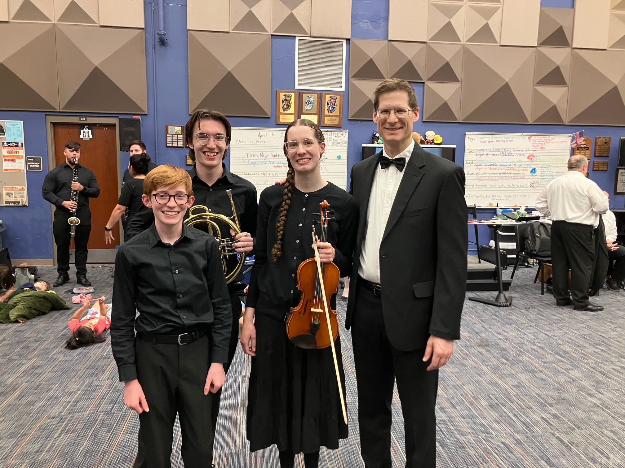 Young musicians with their instruments standing beside an adult conductor in a rehearsal room