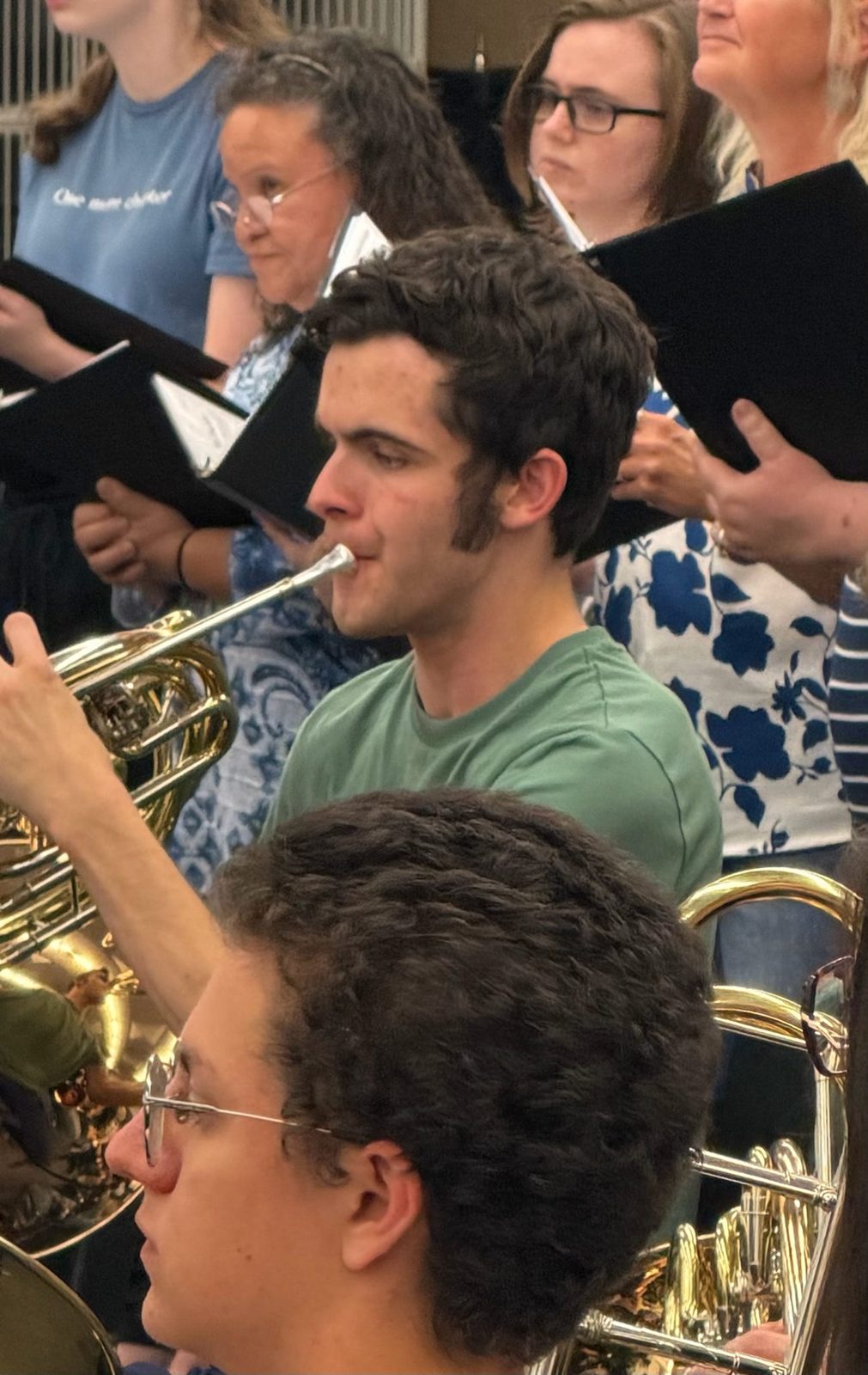 A horn player in rehearsal surrounded by singers