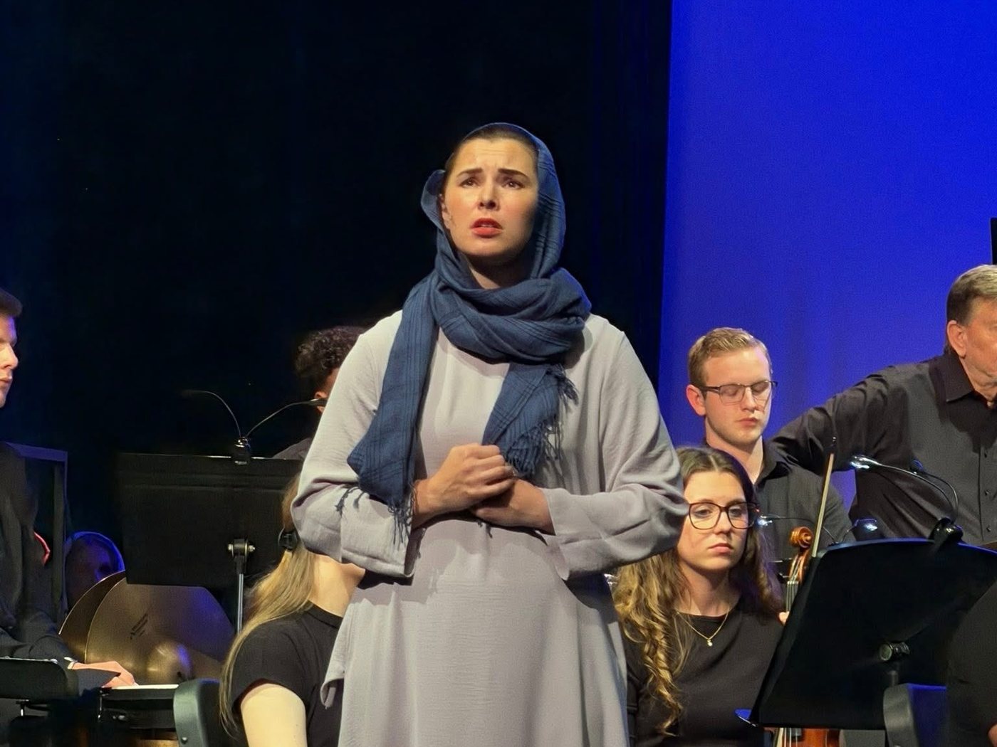 A soloist in a blue headscarf singing on stage in front of the orchestra