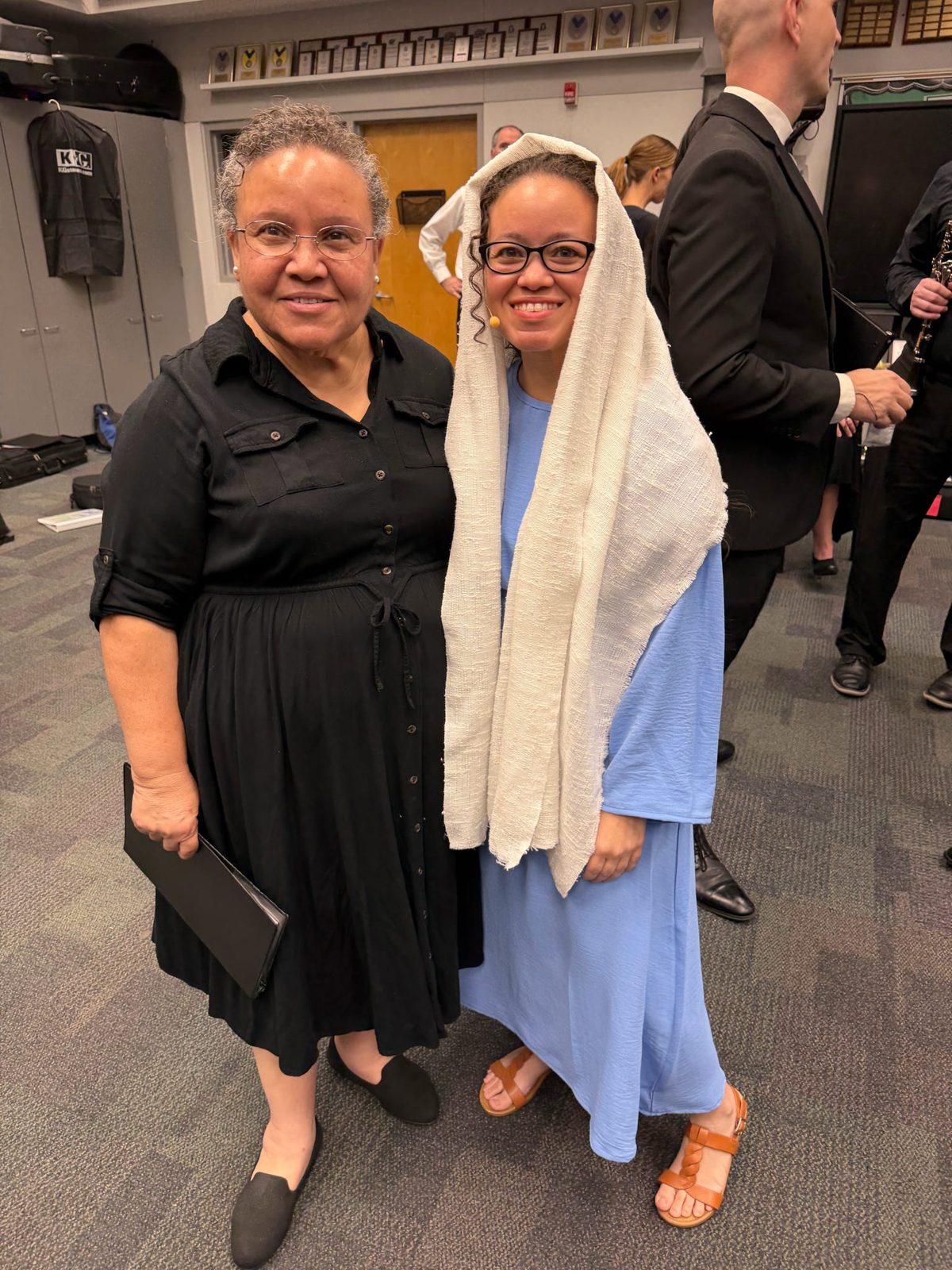 Two performers, one in costume, smiling together backstage
